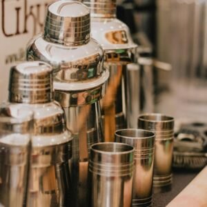 Close-up of sleek metal cocktail shakers and cups lined up in a bar setting.